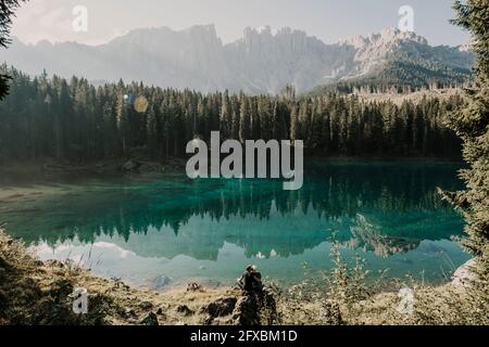 Ehepaar sitzt auf Felsformation am Karersee inmitten von Bäumen in Südtirol, Italien Stockfoto