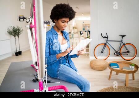 Afro-Frau beim Anschauen eines Tutorials auf einem digitalen Tablet, während sie das Fahrrad zu Hause repariert Stockfoto