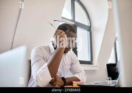 Besorgt männlichen professionellen halten Brillen, während Blick auf Laptop im Büro Stockfoto