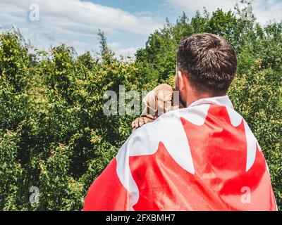 Attraktiver Mann hält einen charmanten Welpen auf einem Hintergrund von blauem Himmel an einem klaren, sonnigen Tag. Im Freien, Nahaufnahme. Nationales Urlaubskonzept Stockfoto