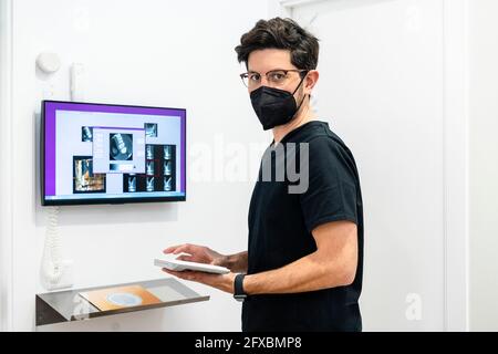 Männlicher Zahnarzt trägt eine schützende Gesichtsmaske mit Computertastatur in der Klinik Stockfoto