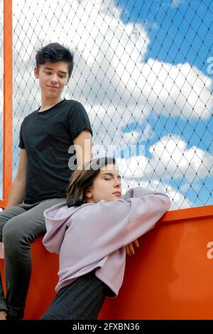 Teenager-Junge, der die Freundin ansieht, die sich auf einem eingezäunten Geländer stützt Stockfoto