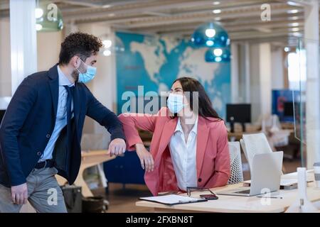 Männliche und weibliche Unternehmer tun Ellenbogenstoß während Pandemie im Büro Stockfoto