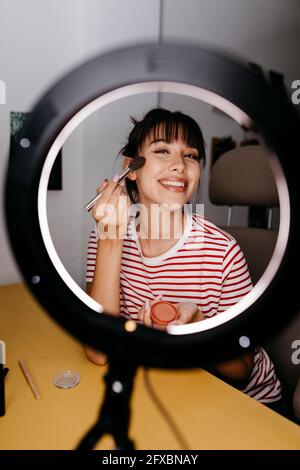 Lächelnde Influencerin, die beim Vlogging im Studio Make-up anwendet Stockfoto