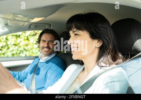 Lächelnde Geschäftsfrau, die mit einem Mann im Auto unterwegs ist Stockfoto