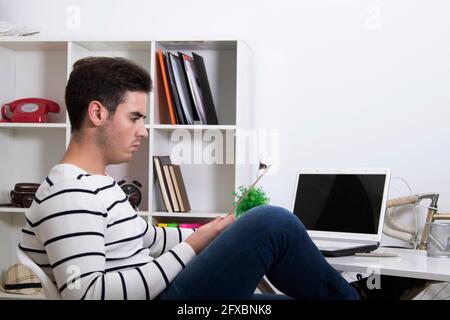Junger Mann, der zu Hause mit einem Laptop auf dem Desktop studiert Computer Stockfoto