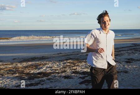 Lächelnder junger Mann, der am Strand läuft Stockfoto