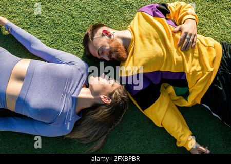 Lächelnder Mann, der während eines sonnigen Tages bei einer Frau auf dem Gras liegt Stockfoto