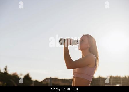 Weibliche Sportlerin trinkt Wasser aus der Flasche an sonnigen Tagen Stockfoto