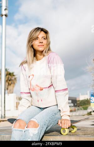 Lächelnde Frau, die im Park auf dem Skateboard sitzt Stockfoto