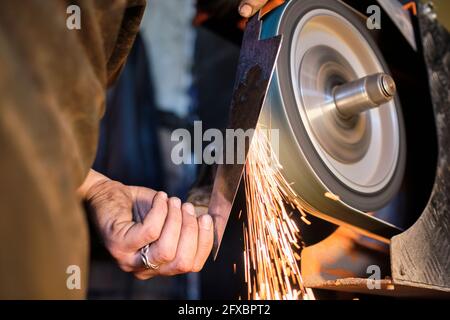 Männlicher Schmied schärft Messer Form Metall auf Schleifer in der Werkstatt Stockfoto