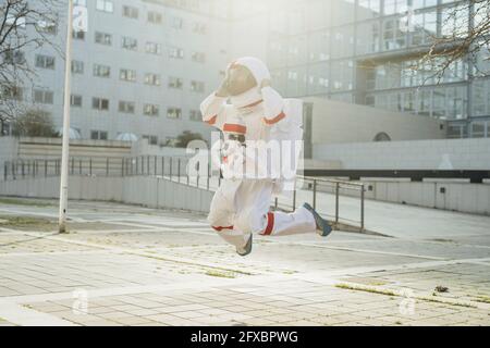 Junge Astronautin im Weltraumanzug springt auf dem Fußweg in der Nähe von Gebäuden in der Stadt Stockfoto