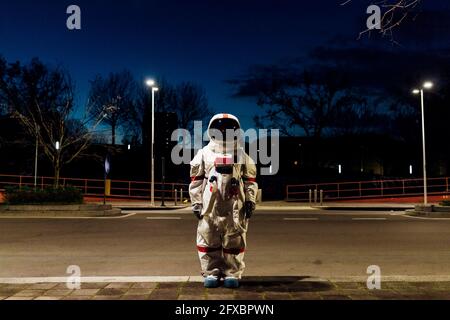 Junge Astronautin im Weltraumanzug, die nachts auf dem Fußweg steht Stockfoto