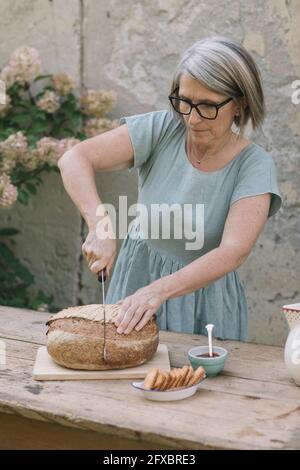 Reife Frau, die auf dem Tisch im Hinterhof Brot schneidet Stockfoto