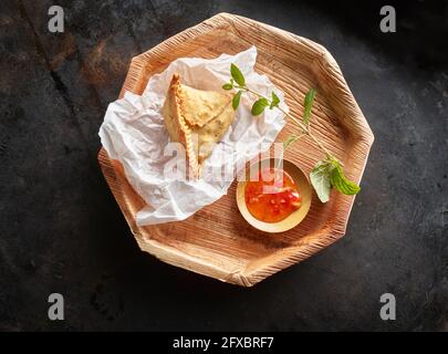 Studioaufnahme eines hölzernen Untersetzer mit Samosa-Knödel und Schüssel mit Chilisauce Stockfoto
