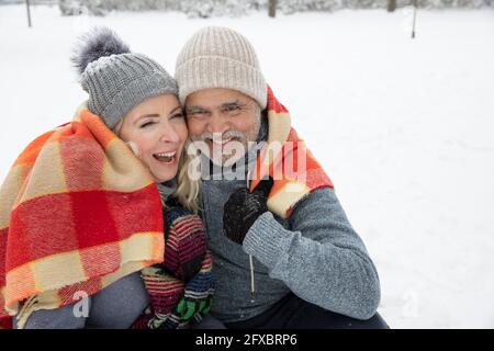 Lächelndes Paar, das im Winter in eine Decke gehüllt wurde Stockfoto