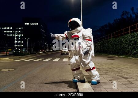 Weibliche Astronautin im Raumanzug, die nachts auf einem Fußpfad in der Nähe der Straße steht Stockfoto