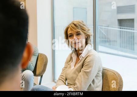 Weibliche Fachleute diskutieren mit Kollegen, während sie in der Bürolobby sitzen Stockfoto