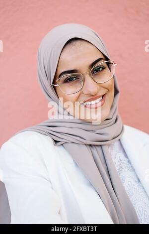 Lächelnde Frau mit Brille, die vor einer rosa Wand steht Stockfoto