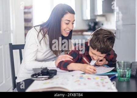 Lächelnde Mutter, die dem Sohn bei Hausaufgaben zu Hause hilft Stockfoto