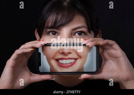Lächelnde schöne Frau, die Selfie über das Smartphone auf schwarzem Hintergrund nimmt Stockfoto