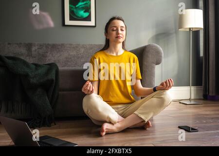 Junge Frau meditiert, während sie zu Hause sitzt Stockfoto