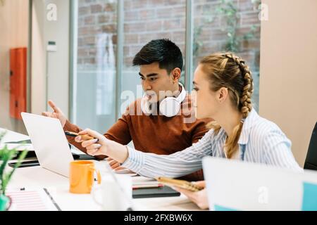 Männliche und weibliche Unternehmer diskutieren über Laptop im Büro Stockfoto