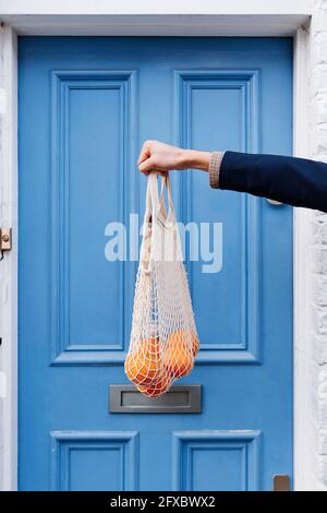 Mann, der einen Beutel mit Orangen vor der blauen Tür hält Stockfoto