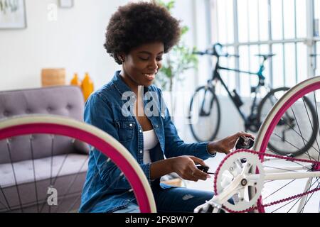 Lächelnde junge Frau, die zu Hause Fahrrad repariert Stockfoto