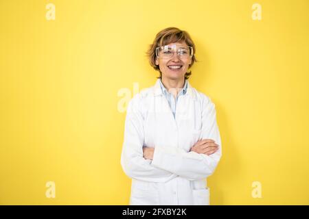 Weibliche Profi trägt schützende Arbeitskleidung, die vor der gelben Wand steht Stockfoto