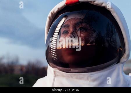 Nachdenkliche Astronautin, die bei Sonnenuntergang mit Weltraumhelm wegschaut Stockfoto