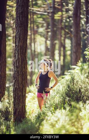 Fröhliche Frau mit Händen an der Hüfte, die im Wald wegschaut Stockfoto