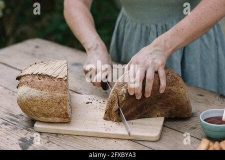 Reife Frau, die Brot auf dem Tisch aufschneiden Stockfoto