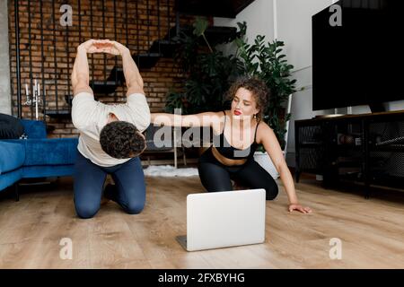 Fit jungen Mann macht Sport zu Hause mit Laptop auf dem Boden liegend mit Freundin Unterstützung helfenden Freund, sportliche weibliche Ausbildung Mann bei Stockfoto