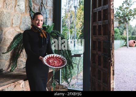 Junge Besitzerin hält Teller mit rotem Fleisch, während sie im Restaurant steht Stockfoto