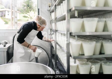 Reifer männlicher Unternehmer, der Käsebehälter im Regal im Lagerraum anordnete Stockfoto