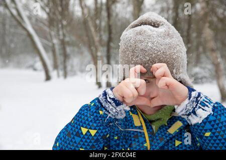 Junge in warmer Kleidung, die im Winter herzförmig macht Stockfoto