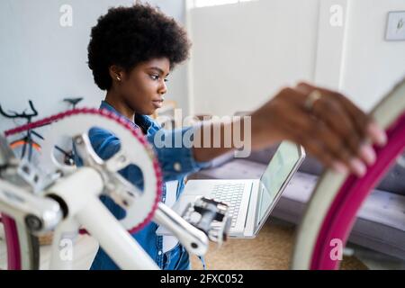 Afro-Frisur Frau beobachten Tutorial auf Laptop, während Reparatur Fahrrad zu Hause Stockfoto