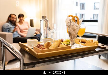 Reifes Paar auf dem Sofa sitzend mit Frühstück im Vordergrund im Hotelzimmer Stockfoto