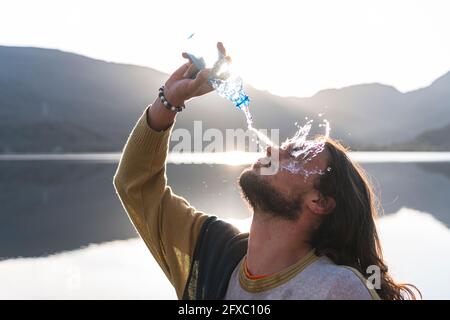 Mann gießt Wasser auf das Gesicht mit einer Flasche in der Nähe des Sees während eines sonnigen Tages Stockfoto