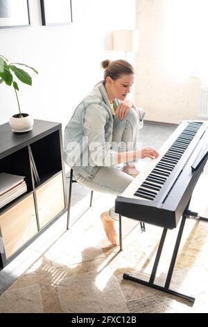 Frau mit mittlerem Erwachsenen übt Klavier, während sie im Wohnzimmer sitzt Stockfoto