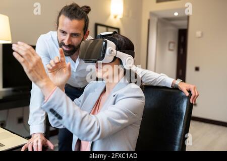 Reife Geschäftsfrau im Virtual-Reality-Simulator von einem männlichen Kollegen im Hotel Stockfoto