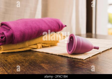 Menstruationstasse auf Bambusmatte am Tisch durch farbige Kleidung Stockfoto