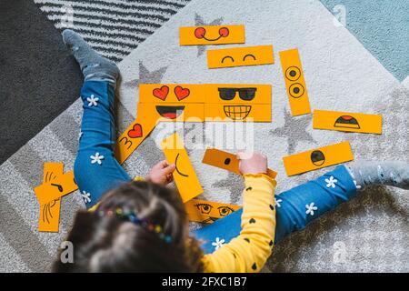 Mädchen spielt mit gelben Papier-Emoticons, während sie zu Hause auf dem Teppich sitzt Stockfoto