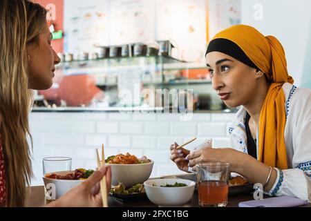 Junge Frauen, die sich beim Essen im Restaurant unterhalten Stockfoto