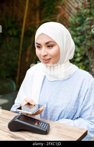 Junge Frau, die im Straßencafé per Smartphone bezahlt Stockfoto