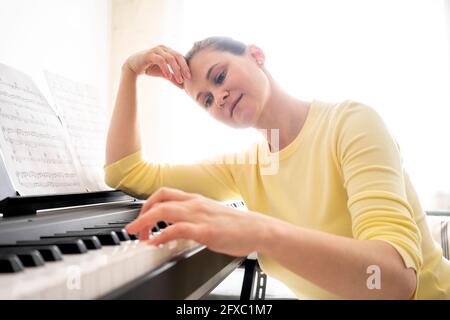 Frau mit Kopf in den Händen, die zu Hause Klavier spielt Stockfoto
