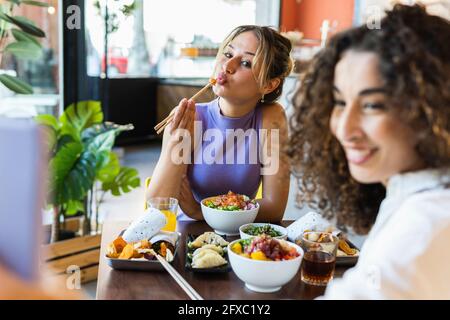 Junge Frau, die Selfie mit einer Freundin gemacht hat, die Essen mit Essstäbchen im Restaurant gegessen hat Stockfoto