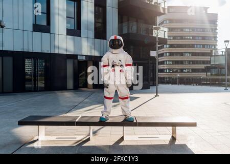 Männlicher Astronaut, der in der Stadt auf der Bank steht Stockfoto