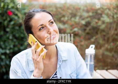 Lächelnde professionelle Frau schaut weg, während sie im Garten telefoniert Stockfoto